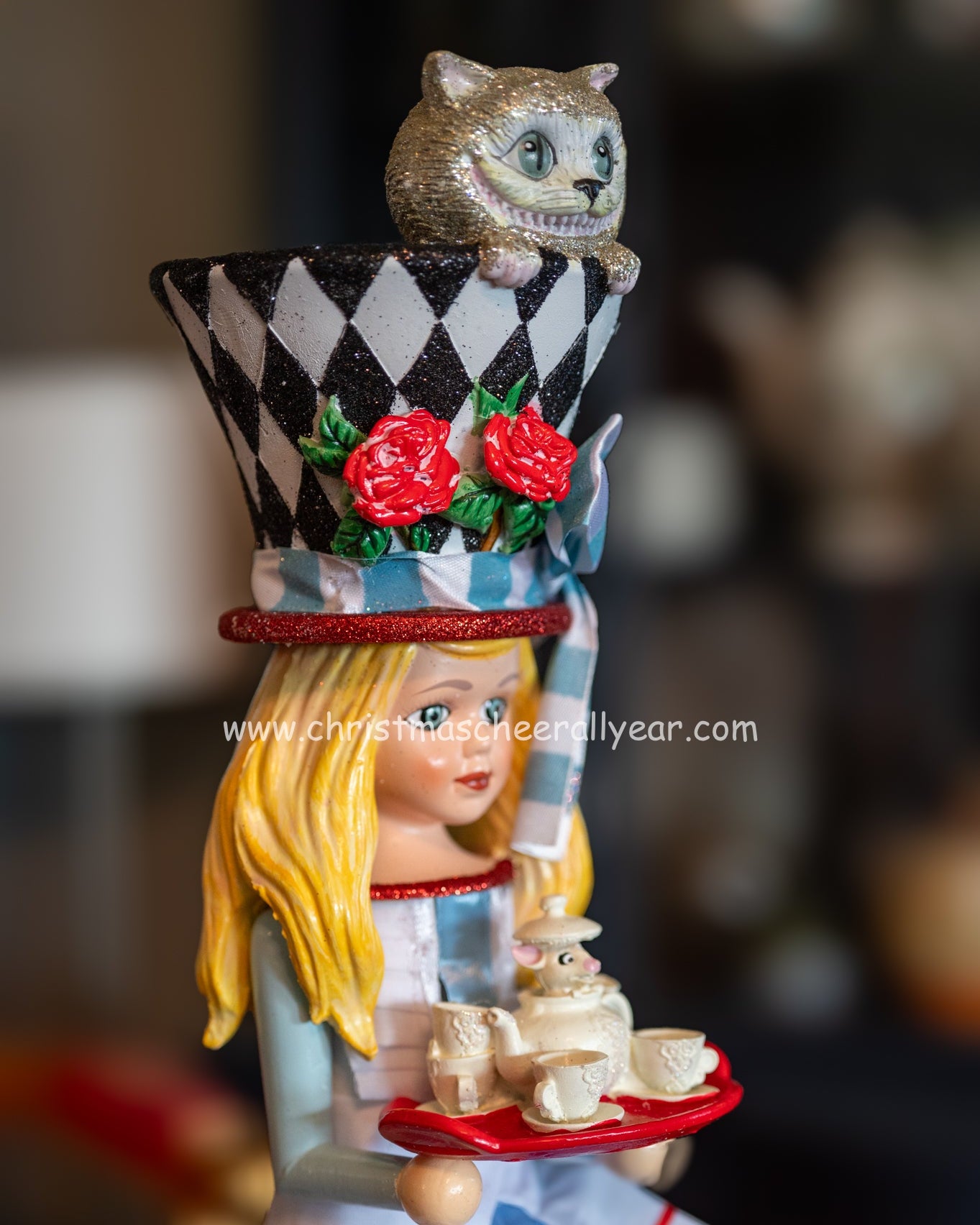 Alice in Wonderland nutcracker with a top hat cheshire cat and tray of items, featuring a blurred background.