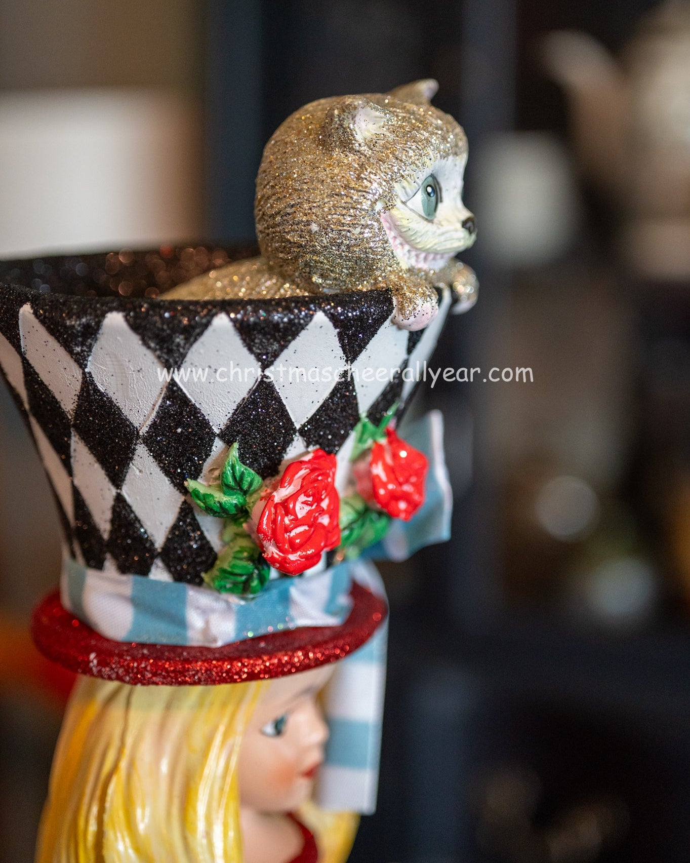 Decorative Alice in wonderland nutcracker character with a checkered hat and red roses on a top hat featuring a cheshire cat on top