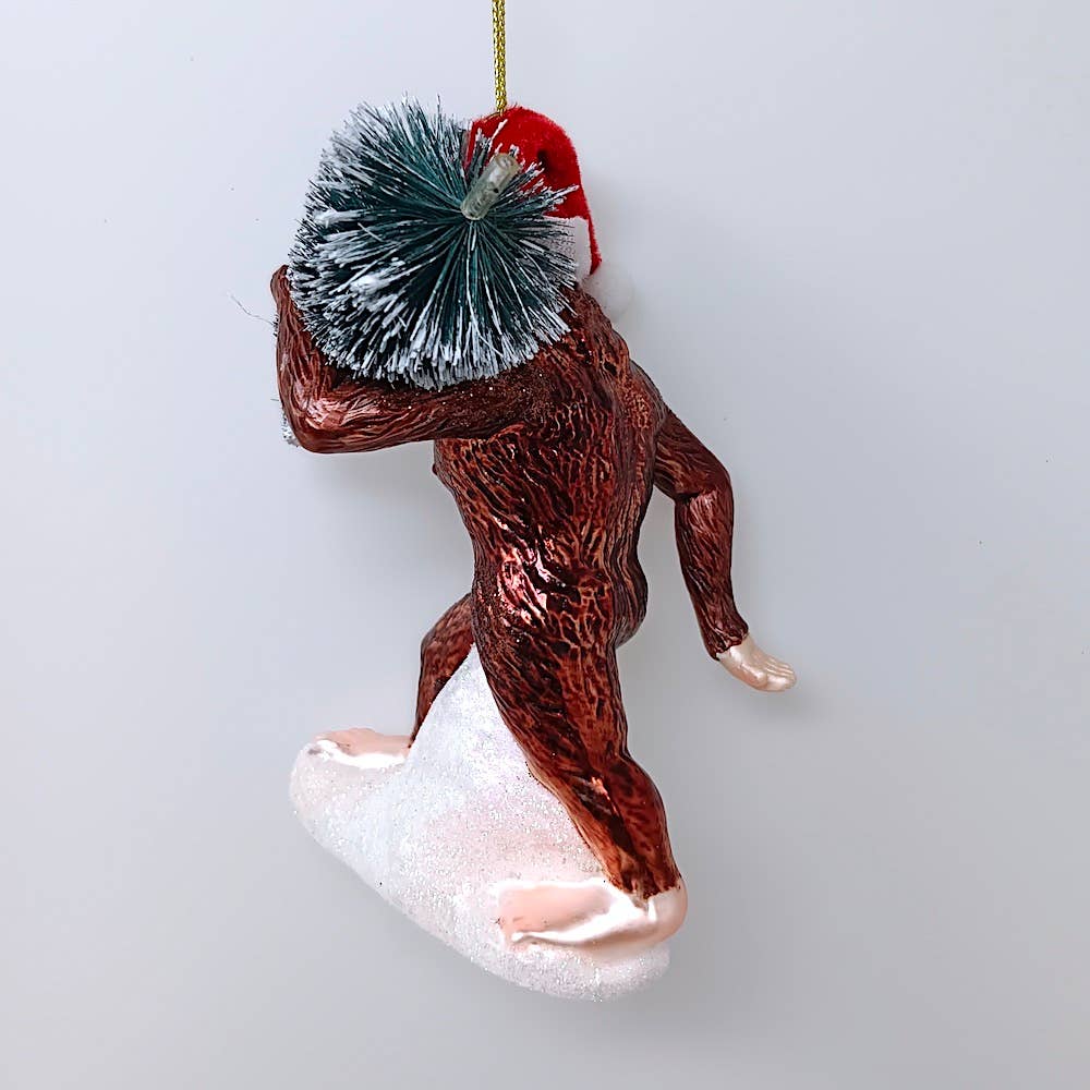 Christmas Cheer All Year Bigfoot glass ornament wearing Santa hat with packages
