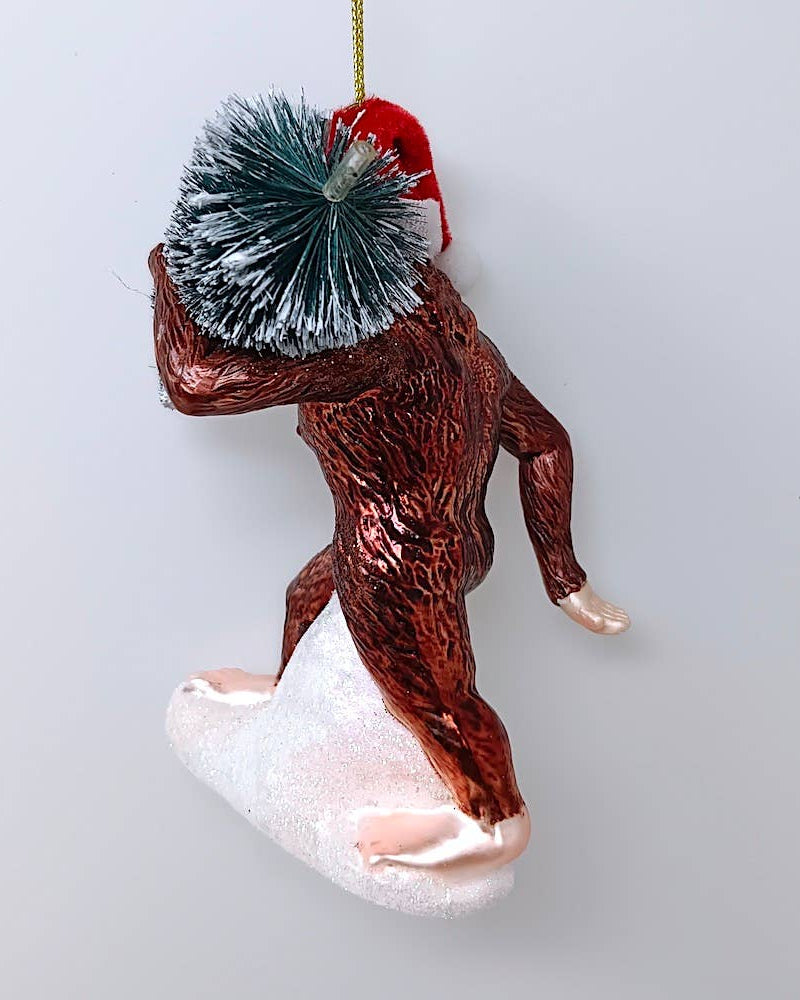 Christmas Cheer All Year Bigfoot glass ornament wearing Santa hat with packages