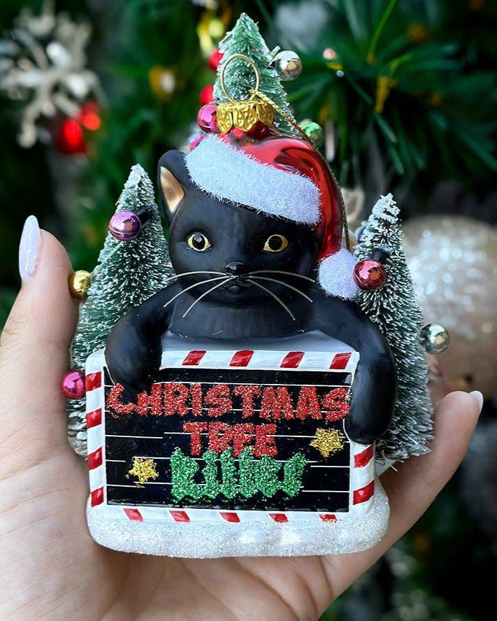 Decorative ornament of a black cat in a Santa hat with Christmas trees and lights.