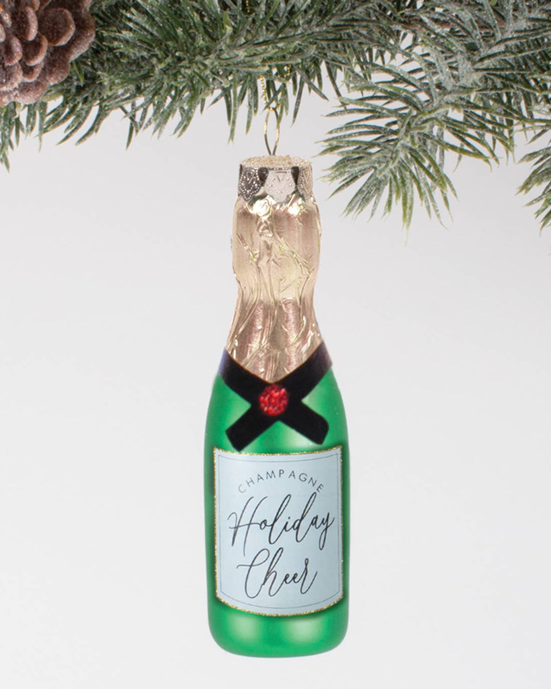 Christmas Cheer All Year Decorative champagne bottle ornament with 'Holiday Cheer' label hanging on a Christmas tree.