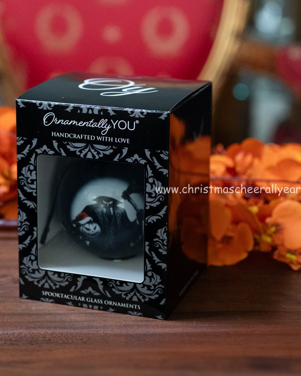 Decorative ornament in a black box with 'Ornamentally YOU' branding, set against a blurred floral background.
