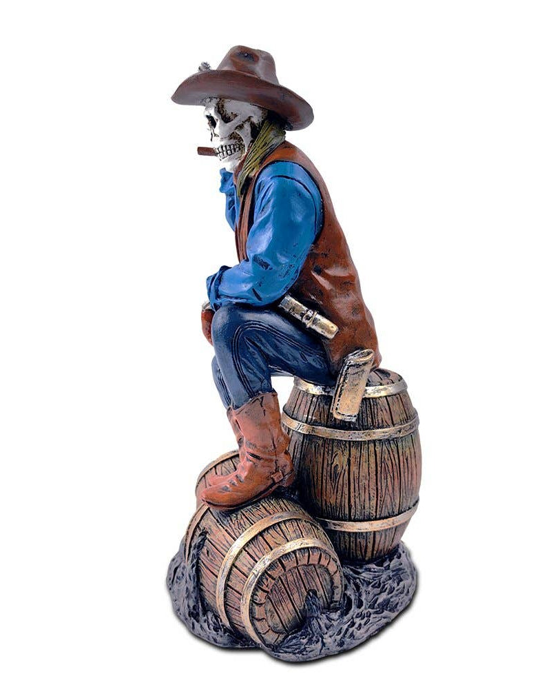 Christmas Cheer All Year handpainted figurine of a Western skeleton gunslinger skeleton wearing a cowboy hat, blue shirt, and brown vest, sitting on a barrel, holding a revolver, with details on the holster and boots.