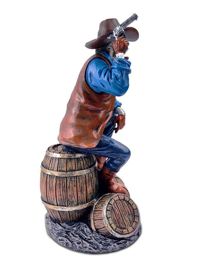 Christmas Cheer All Year handpainted figurine of a Western skeleton gunslinger skeleton wearing a cowboy hat, blue shirt, and brown vest, sitting on a barrel, holding a revolver, with details on the holster and boots.