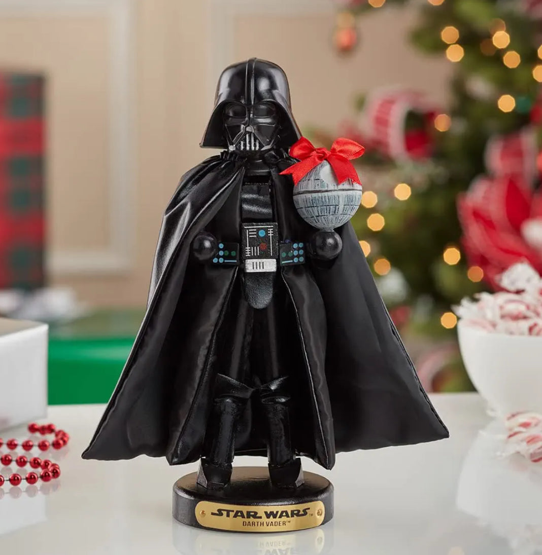 Christmas Cheer All Year A 10-inch tall Star Wars Darth Vader nutcracker figurine, featuring the character in his iconic black helmet and cape, holding a Death Star wrapped in a bow, standing on a base with a Star Wars logo from Kurt Adler