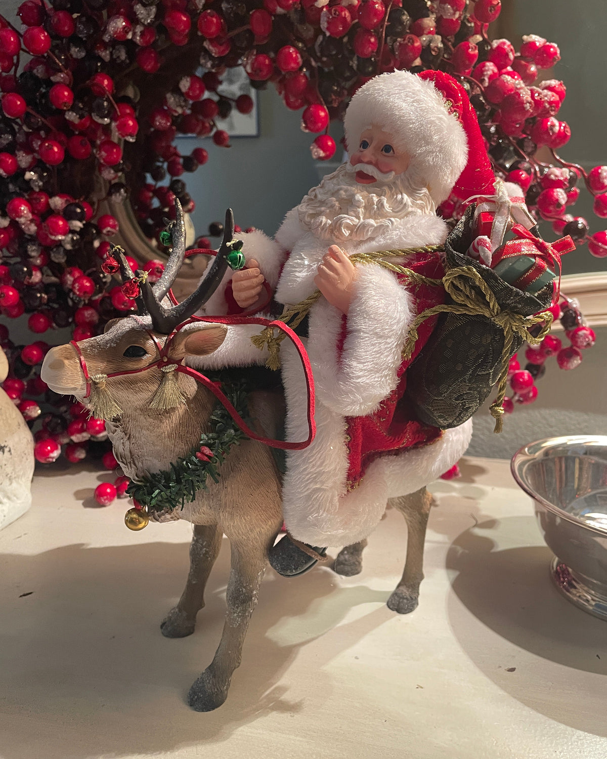 Christmas Cheer All Year 11.5" Fabriche Santa on Reindeer Figurine by Kurt Adler  wearing a red suit with white fur trim, a red hat, and a sack, sitting on a reindeer