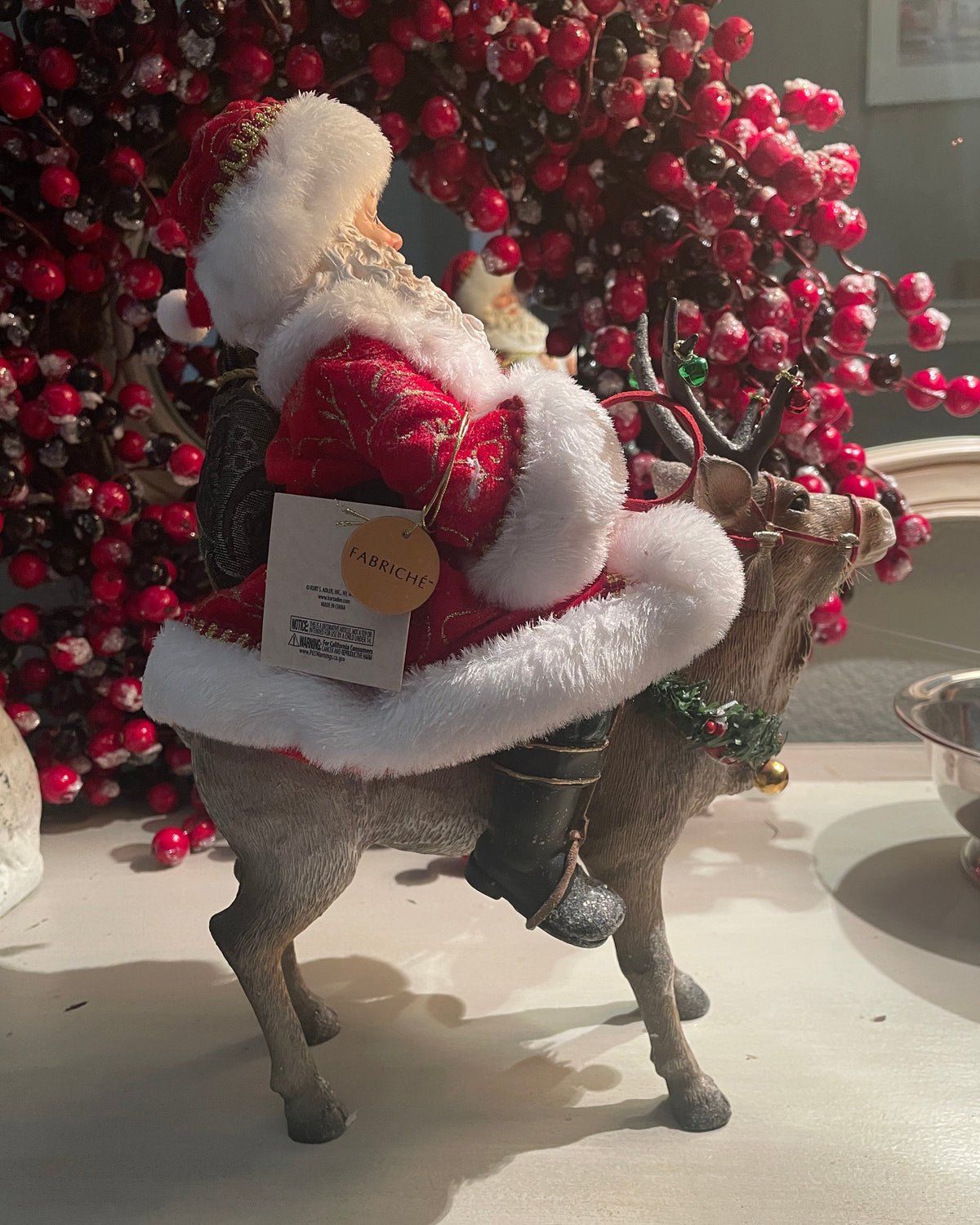 Christmas Cheer All Year 11.5" Fabriche Santa on Reindeer Figurine by Kurt Adler  wearing a red suit with white fur trim, a red hat, and a sack, sitting on a reindeer