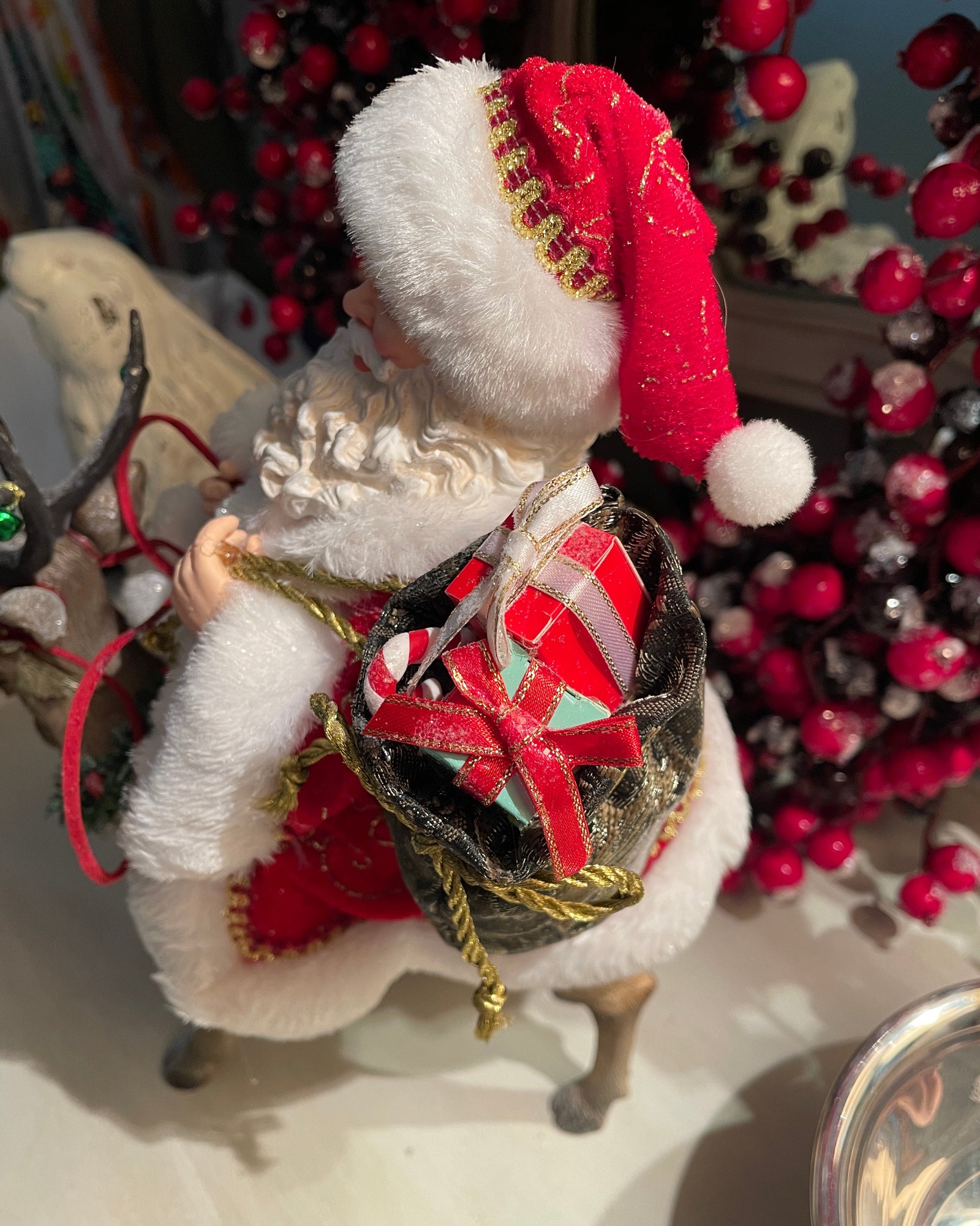 Christmas Cheer All Year 11.5" Fabriche Santa on Reindeer Figurine by Kurt Adler  wearing a red suit with white fur trim, a red hat, and a sack, sitting on a reindeer