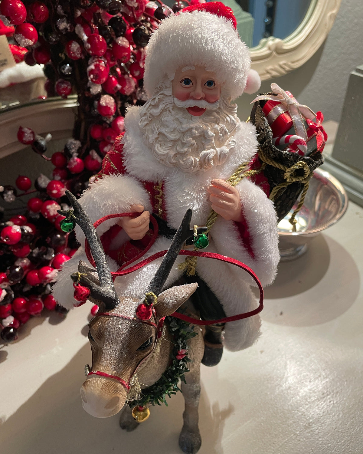 Christmas Cheer All Year 11.5" Fabriche Santa on Reindeer Figurine by Kurt Adler  wearing a red suit with white fur trim, a red hat, and a sack, sitting on a reindeer