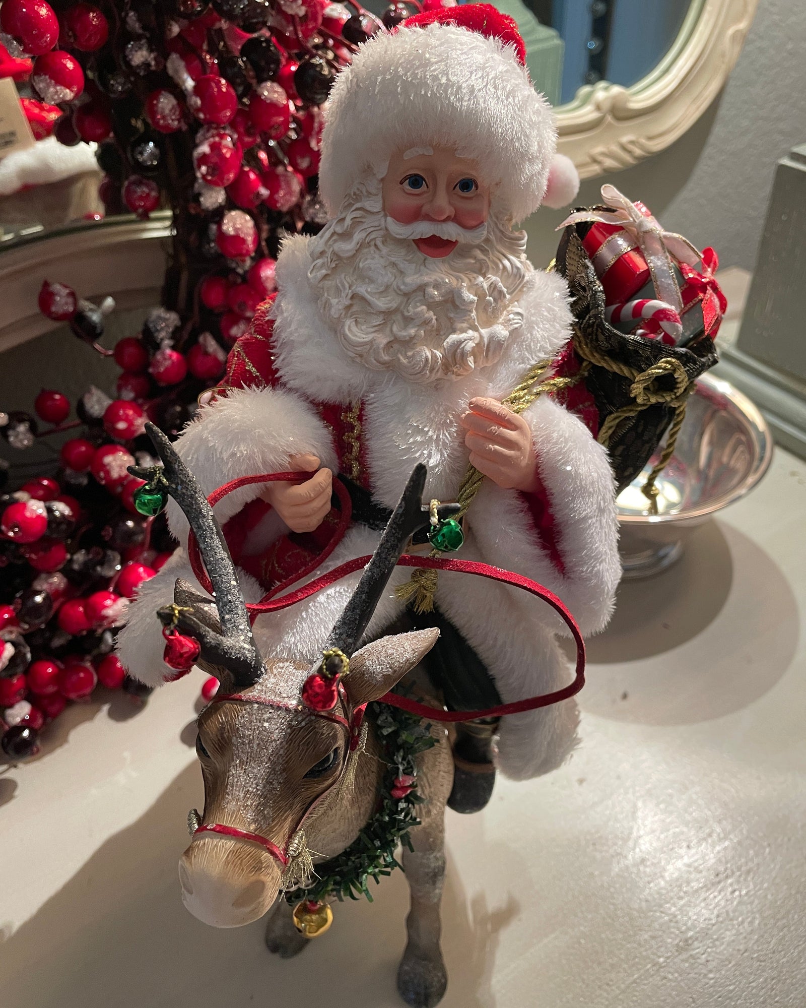 Christmas Cheer All Year 11.5" Fabriche Santa on Reindeer Figurine by Kurt Adler  wearing a red suit with white fur trim, a red hat, and a sack, sitting on a reindeer
