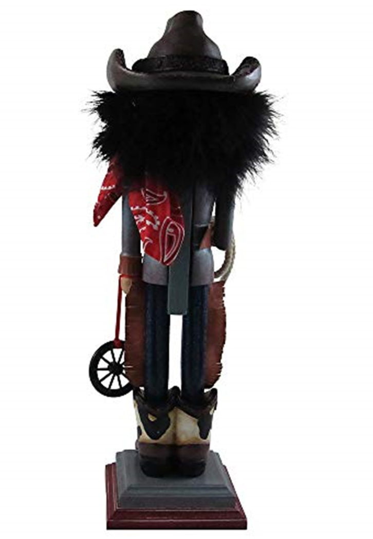 Christmas Cheer All Year A cowboy-themed nutcracker wearing a black wide-brim hat with black buckle detail, a red bandana, jeans with fringe, and brown holstein cowboy boots, standing on a small pedestal