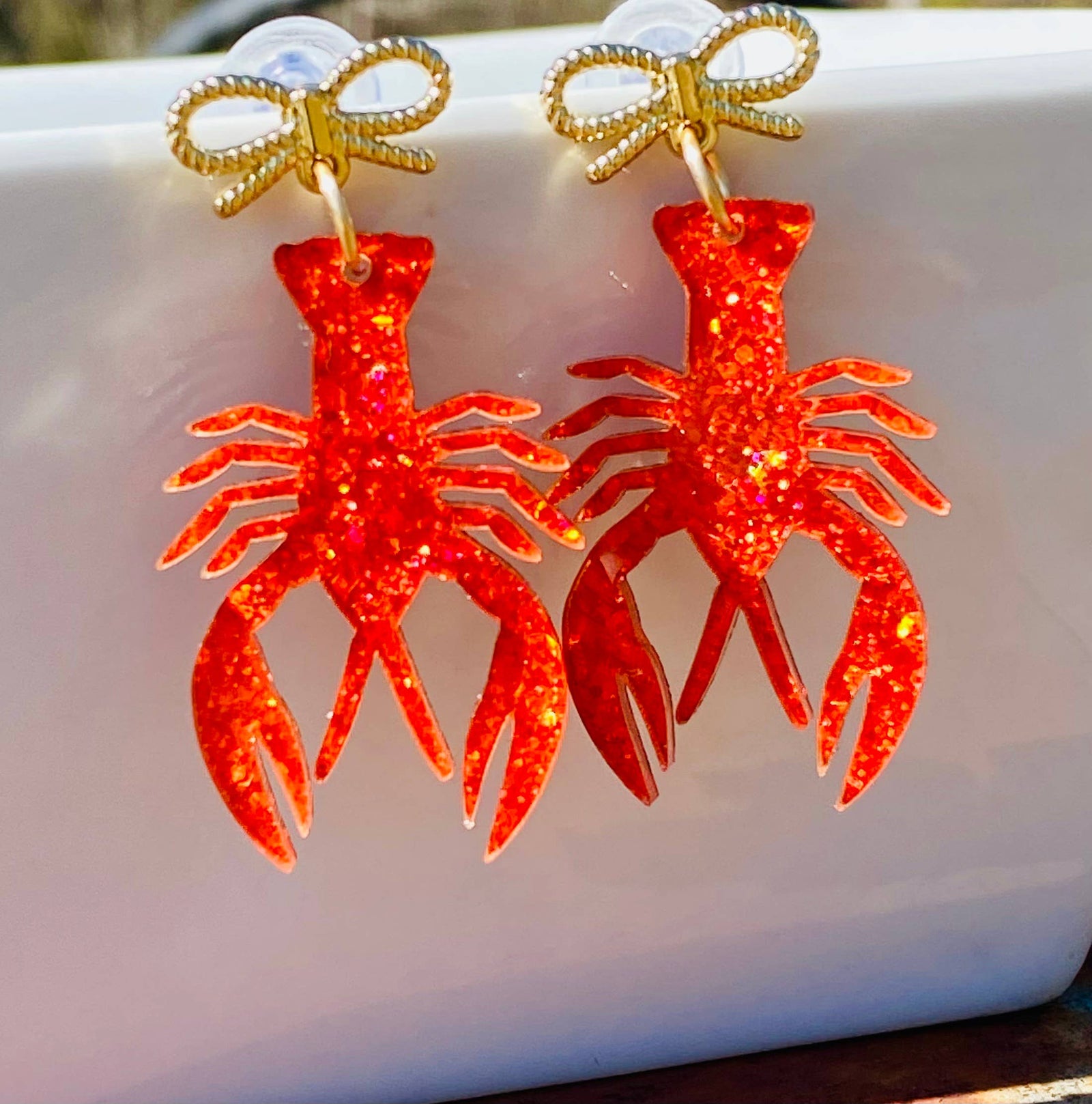 Red lobster-shaped earrings with gold bows on a light blue background