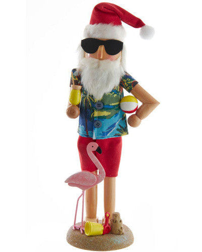 Beach Santa Claus nutcracker in beach attire with sunglasses, shirt, shorts, and flamingo toy on a white background.