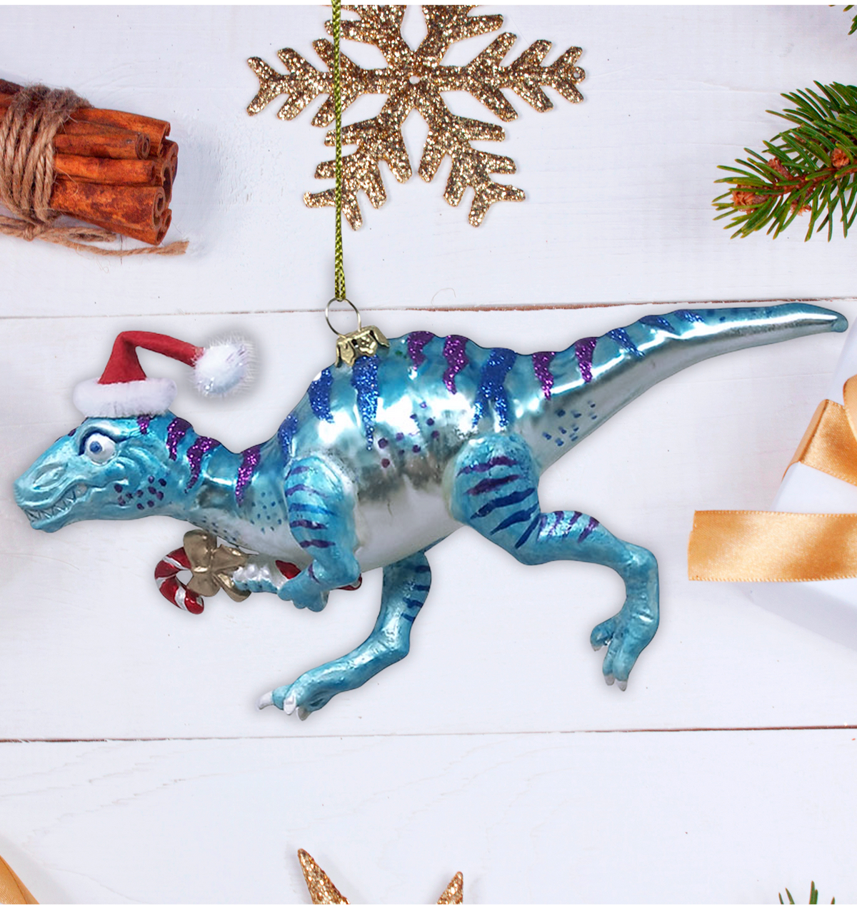 Blue dinosaur Christmas ornament with Santa hat and candy cane on a white surface with festive decorations.