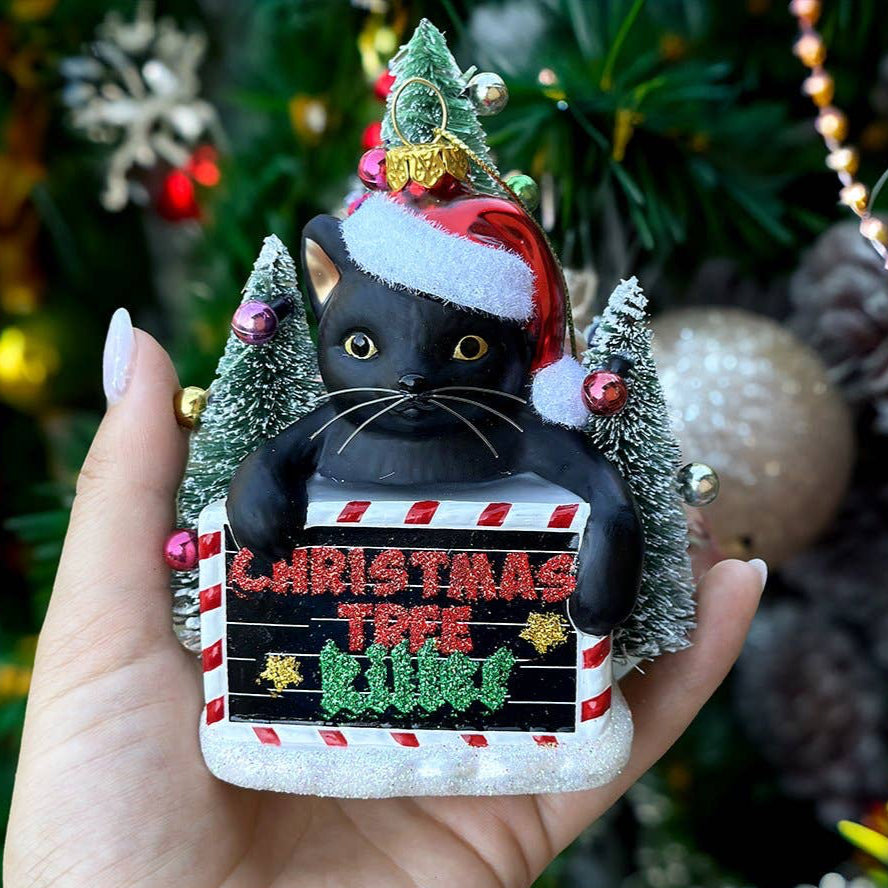 Decorative ornament of a black cat in a Santa hat with Christmas trees and lights.