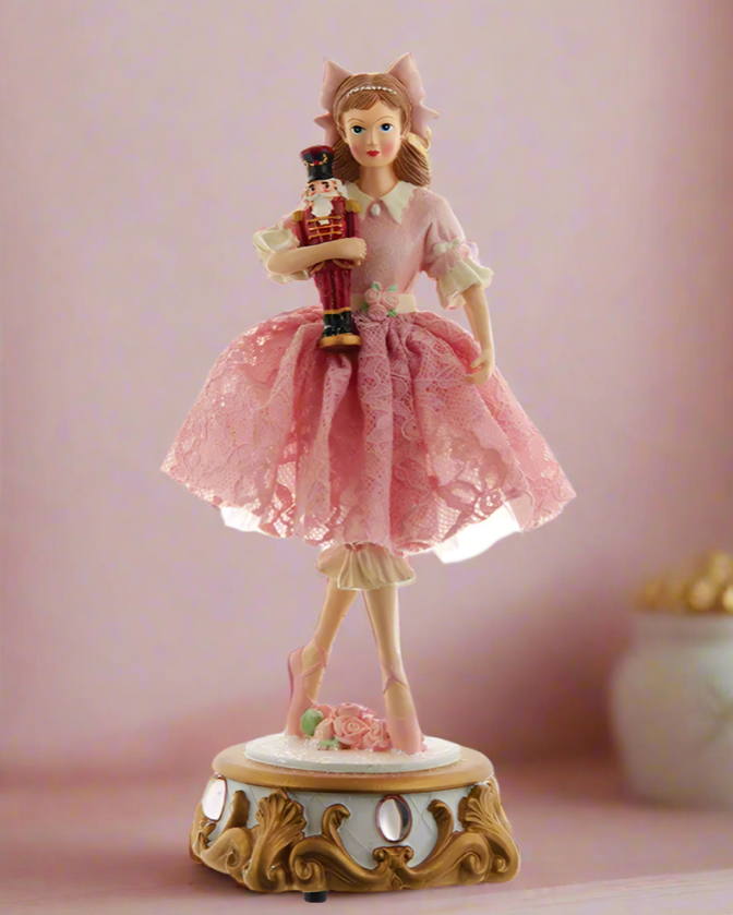 Christmas Cheer All Year Clara holding nutcracker doll in pink lace tutu standing on jeweled base of musical tabletop decor that plays dance of the sugar plum fairy