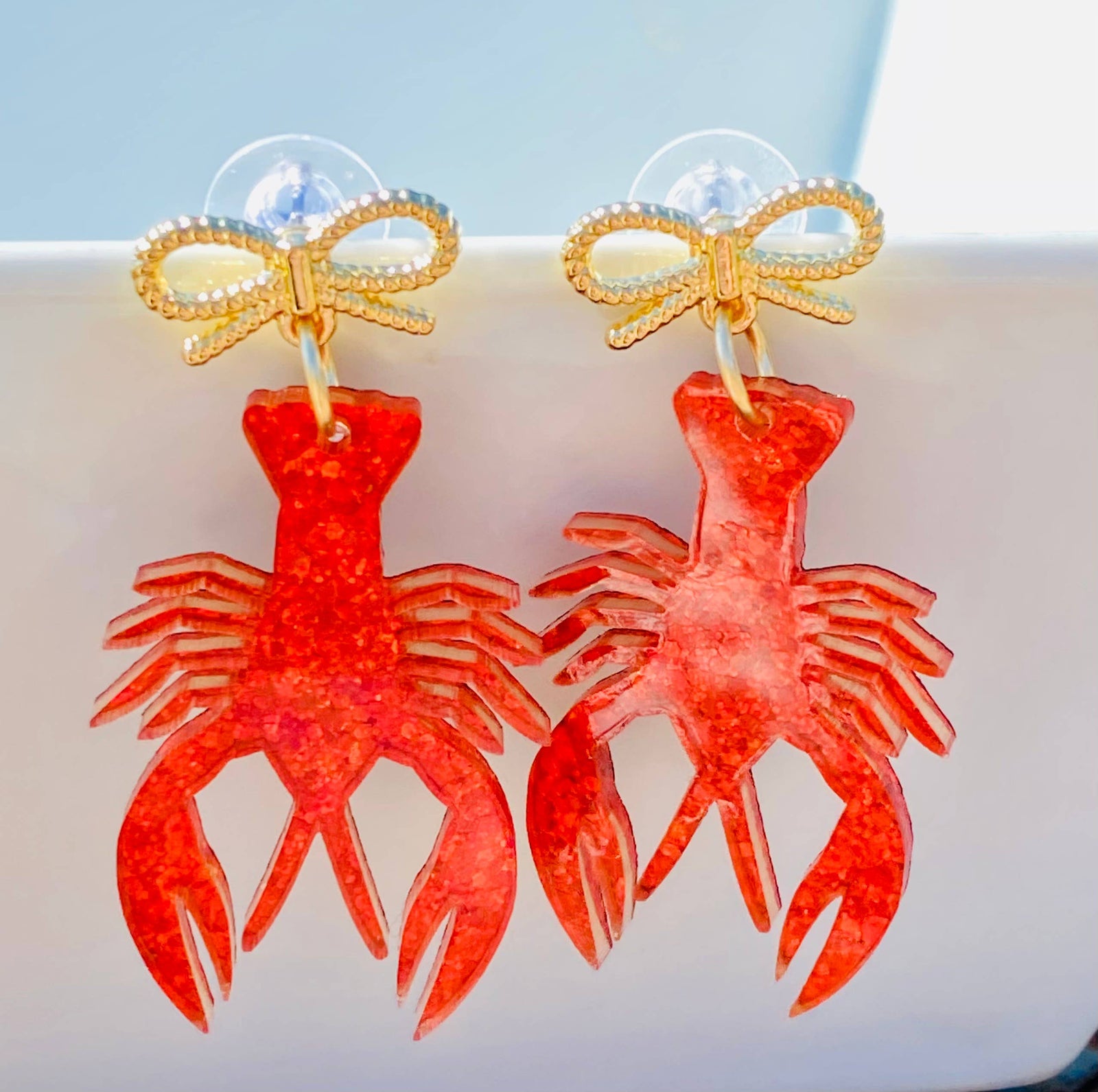Red lobster-shaped earrings with gold bows on a light blue background