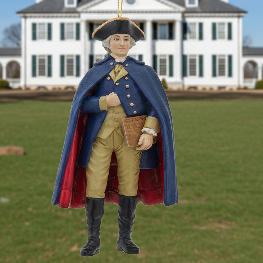 Christmas Cheer All Year 250th USA birthday George Washington Ornament in colonial attire with a blue coat and red interior, holding the U.S. constitution