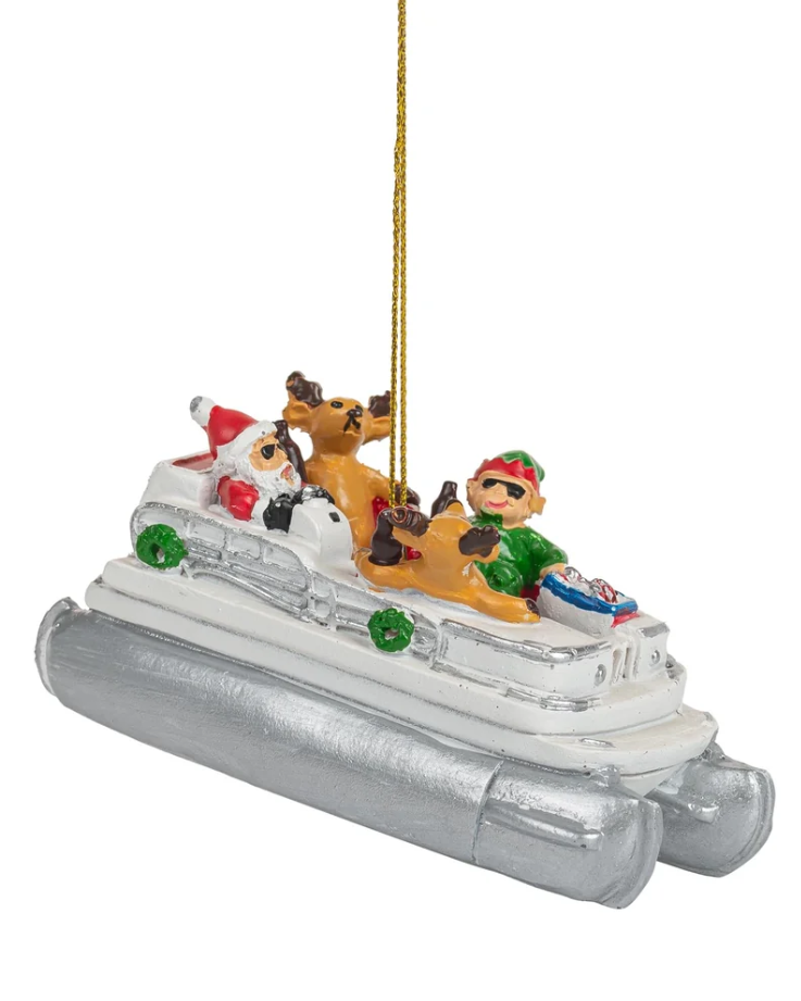 Christmas Cheer All Year ornament shaped like a silver pontoon boat carrying Santa Claus, an elf, a reindeer, and a dog, with a gold hanging loop at the top