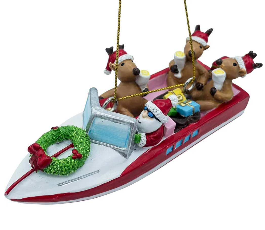 A Christmas ornament shaped like a red and white speedboat carrying Santa Claus and four reindeer, with a green wreath on the bow and small gifts, shown on a plain white background.