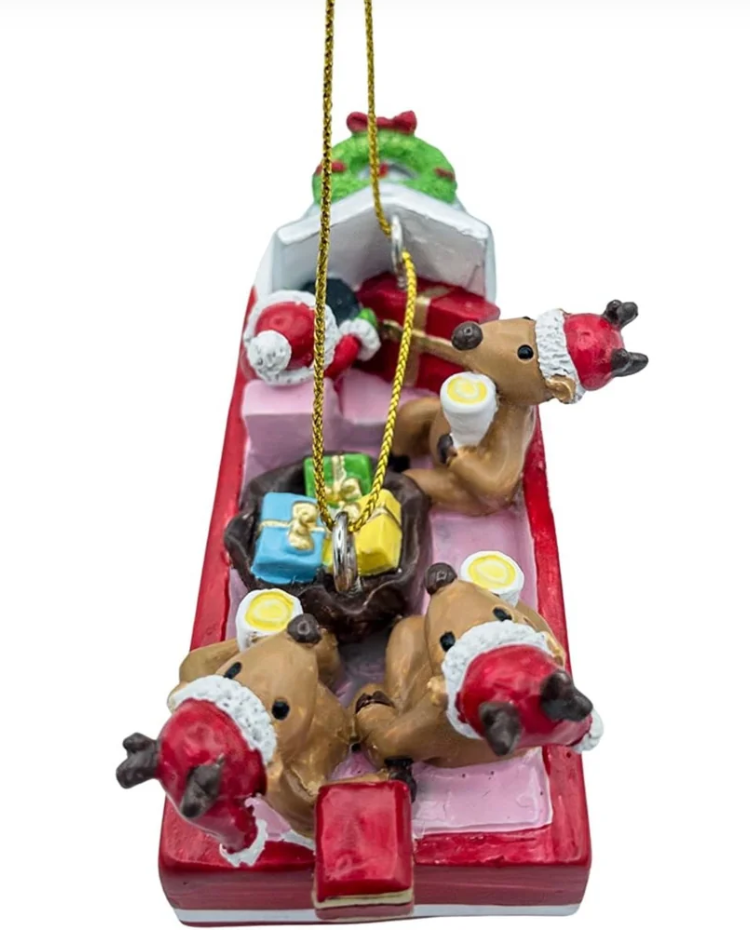 A Christmas ornament shaped like a red sleigh carrying four brown reindeer wearing red and white Santa hats, with a gold hanging string at the top.
