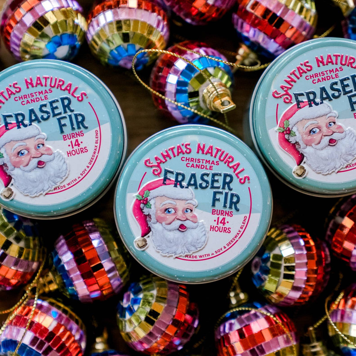 Christmas Cheer All Year Three 'Santa's Naturals' Fraser Fir candles surrounded by colorful Christmas ornaments.