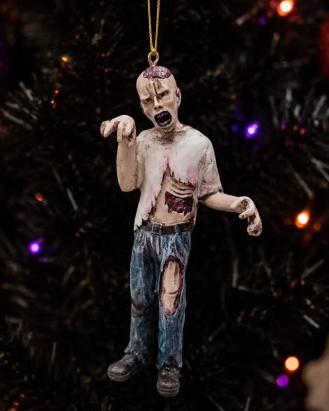 Christmas Cheer All Year A zombie Halloween ornament hanging by a gold string, featuring a distressed, decaying figure with an open shirt, ribs exposed, ripped jeans, bloody leg and a bloody head with skull exposed
