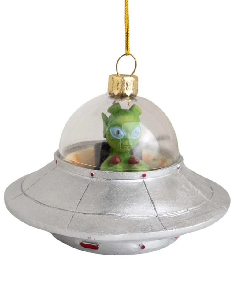 Christmas Cheer All Year silver domed alien spacecraft with green alien inside Christmas ornament hanging from a pine tree branch. The alien is inside a clear domed silver UFO spacecraft with a gold hanging loop