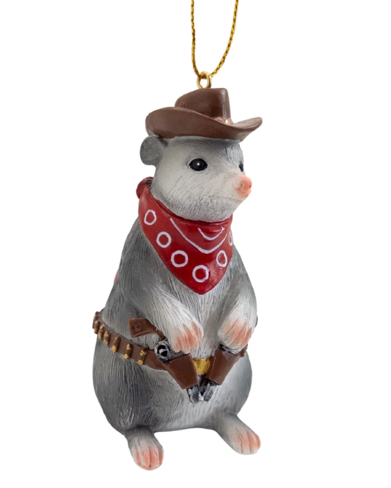 Christmas Cheer All Year cowboy opossum ornament dressed in western attire, wearing a brown cowboy hat, a red bandana with white dots, and a brown holster with a revolver, hanging from a gold string 