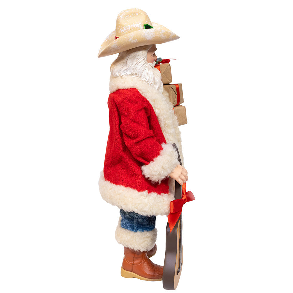 Christmas Cheer All Year Fabriche Cowboy Santa Claus figure holding a guitar and gift boxes on a white background