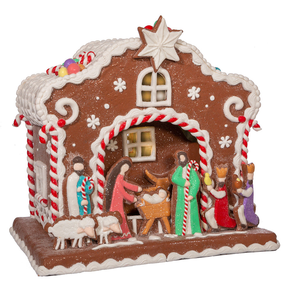 Decorative gingerbread house with nativity scene figures on a white background