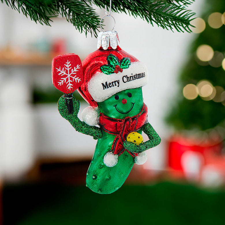 Green Christmas ornament shaped like a foot with a red hat and scarf, hanging on a tree.