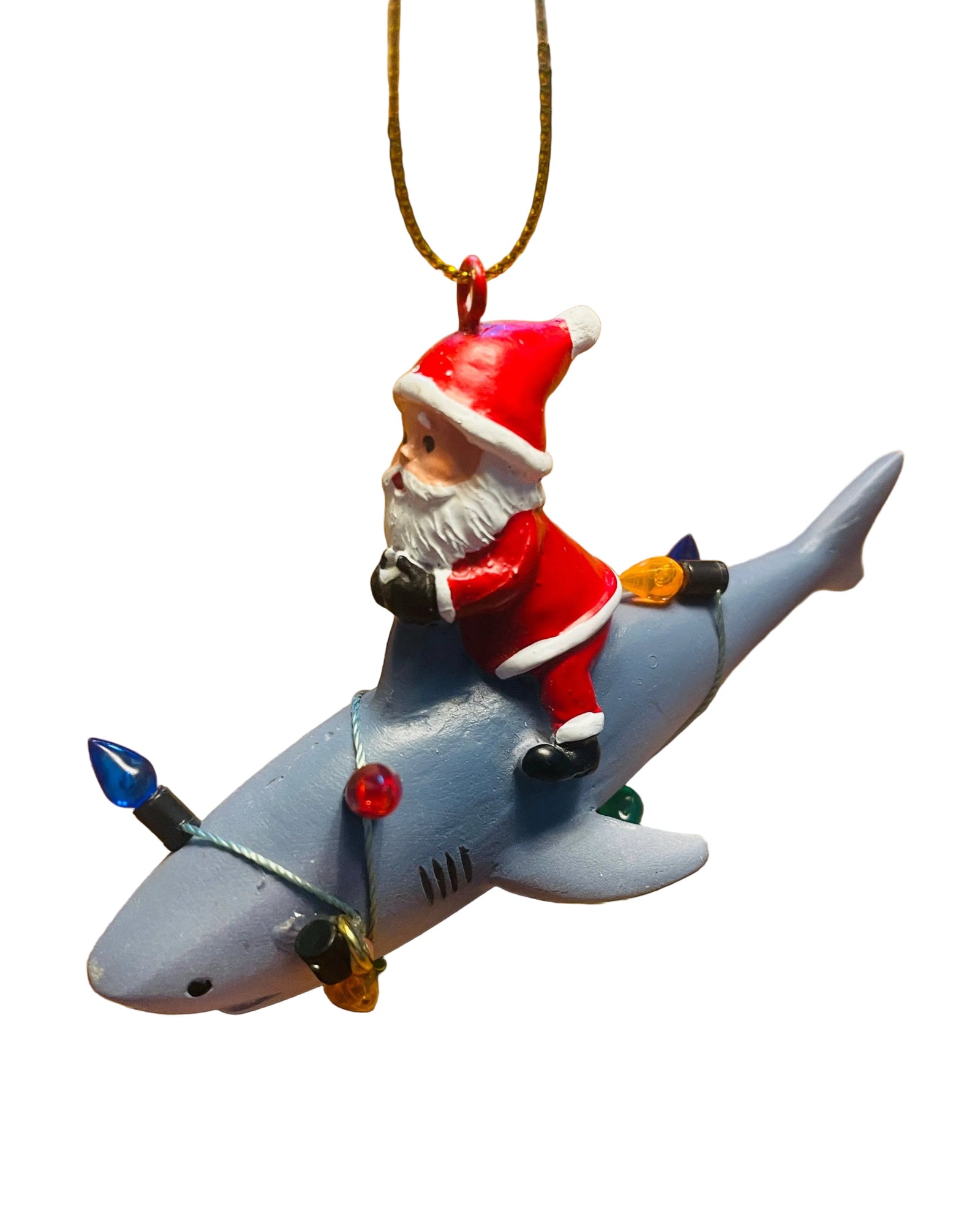 Christmas Cheer All year A Christmas ornament featuring Santa Claus riding a gray shark, hanging from a decorated Christmas tree with gold tinsel and red and gold ornaments.